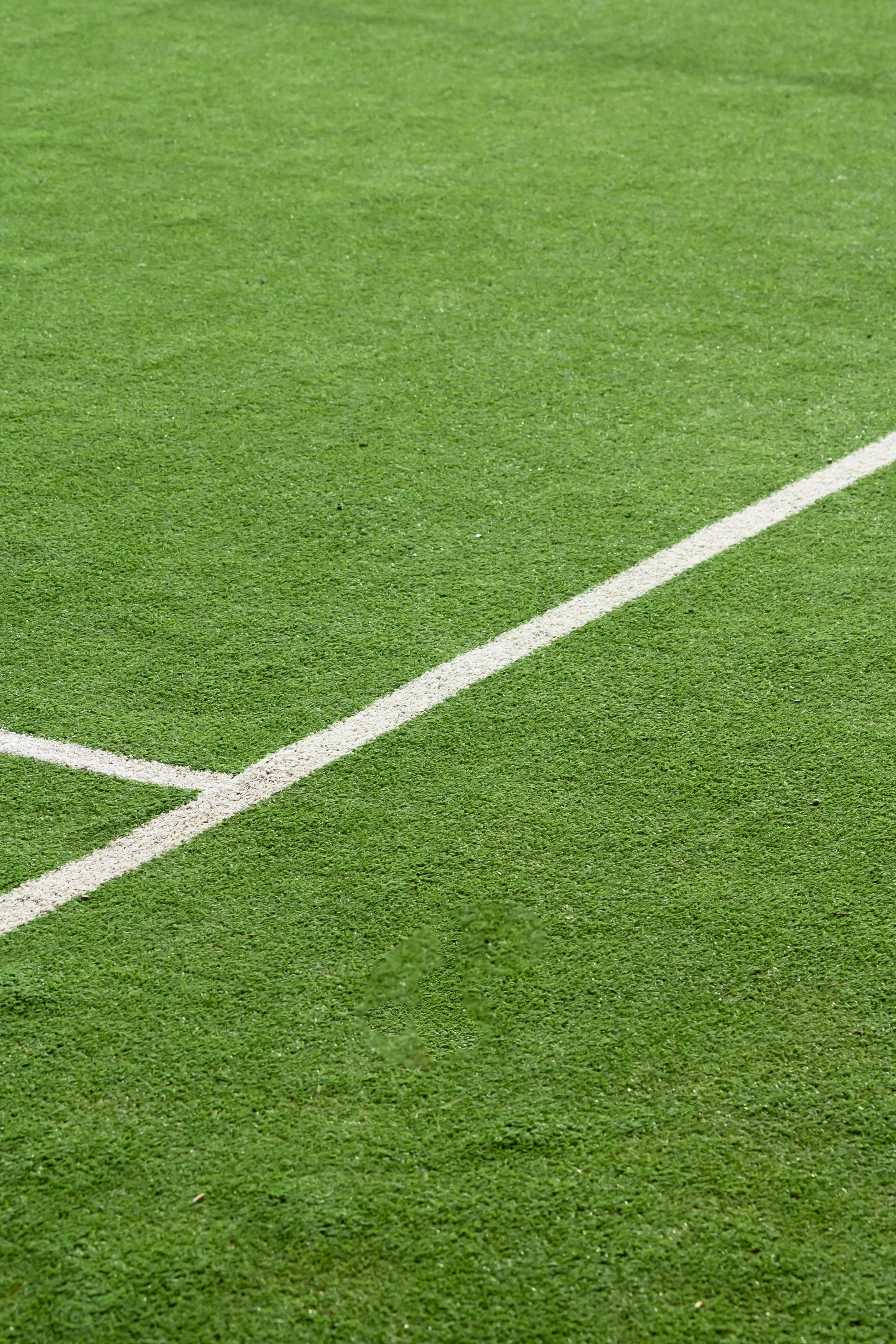 Detalhe real de grama sintética esportiva verde com linhas brancas de marcação.