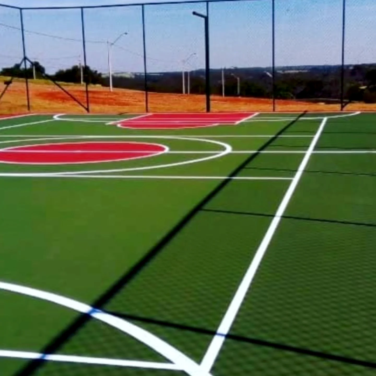 Quadra externa verde com áreas vermelhas e linhas brancas de diferentes modalidades.